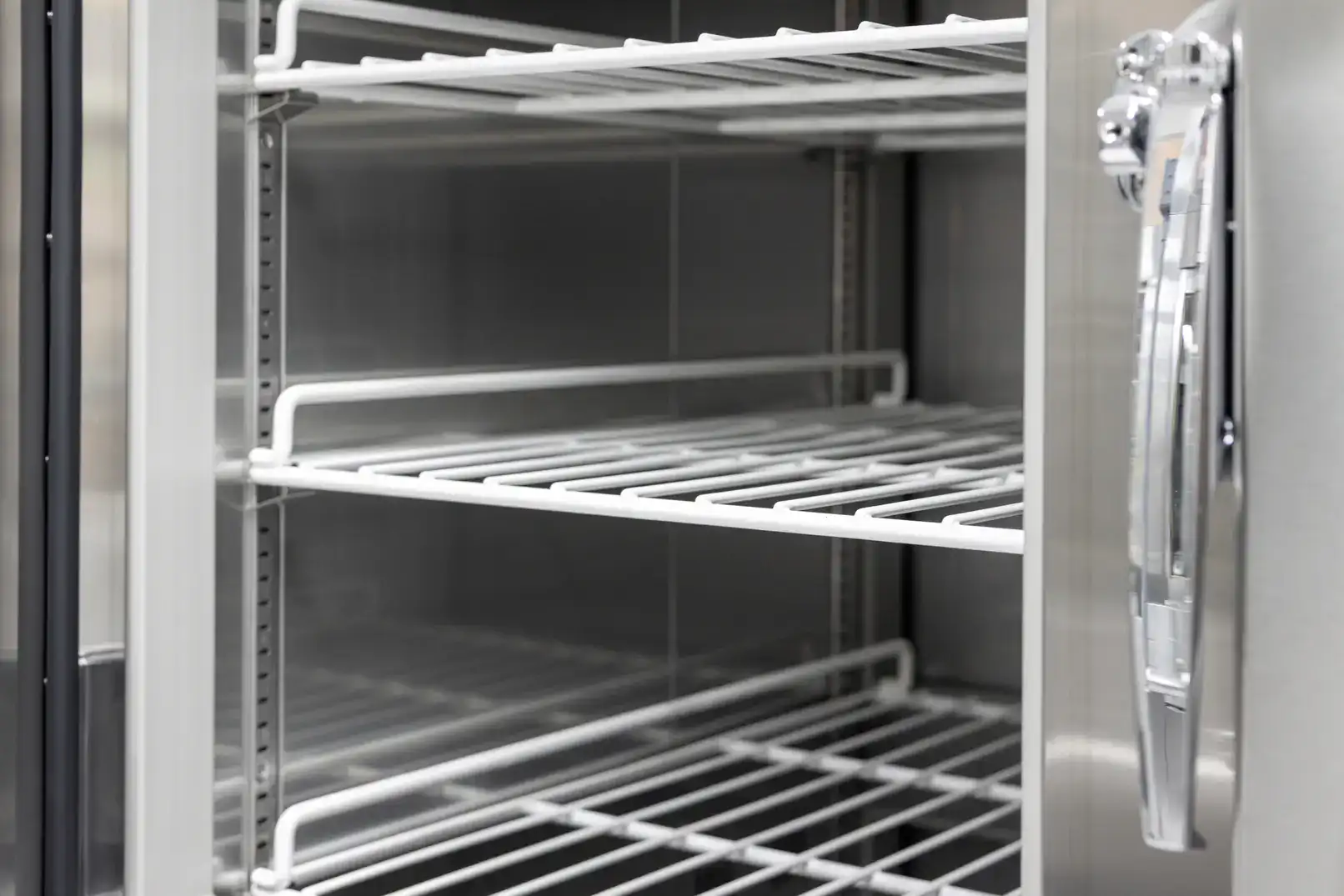 Close-up of empty commercial refrigerator with metal racks for food storage.