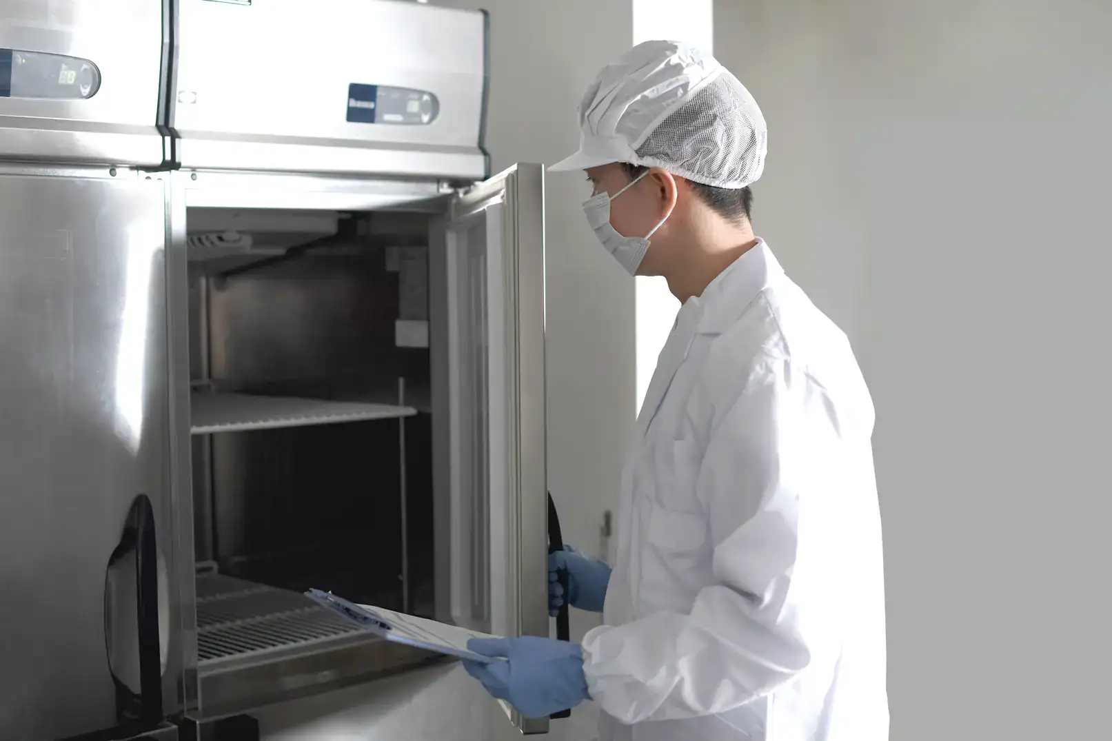 Technician inspecting industrial refrigerator with clipboard in commercial kitchen.